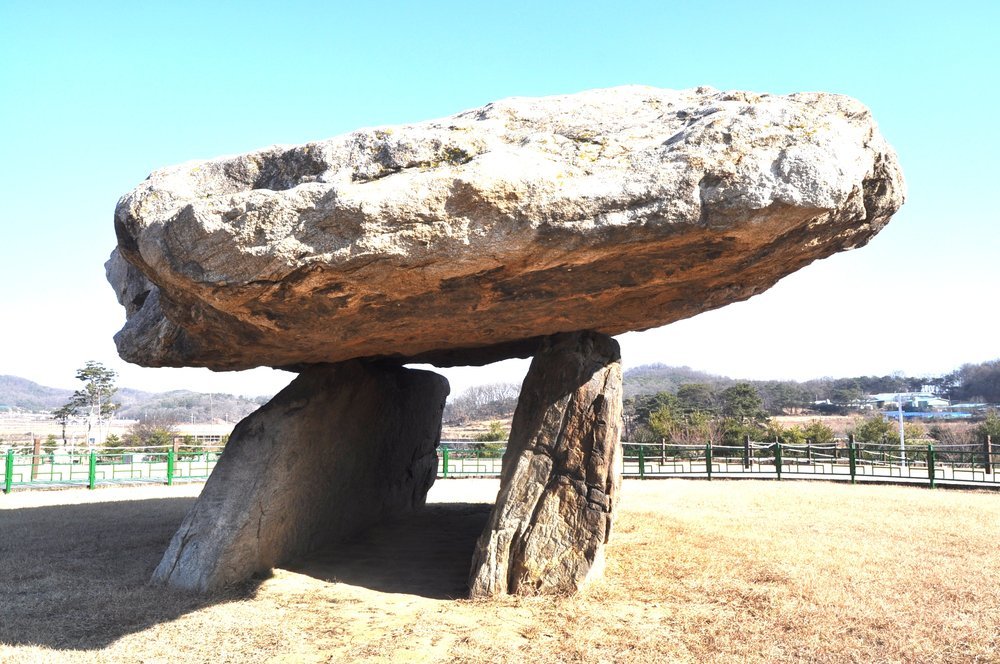 맑은 하늘 아래 마른 잔디 위에서 두 굄돌이 큰 덮개돌을 받친 부근리 지석묘