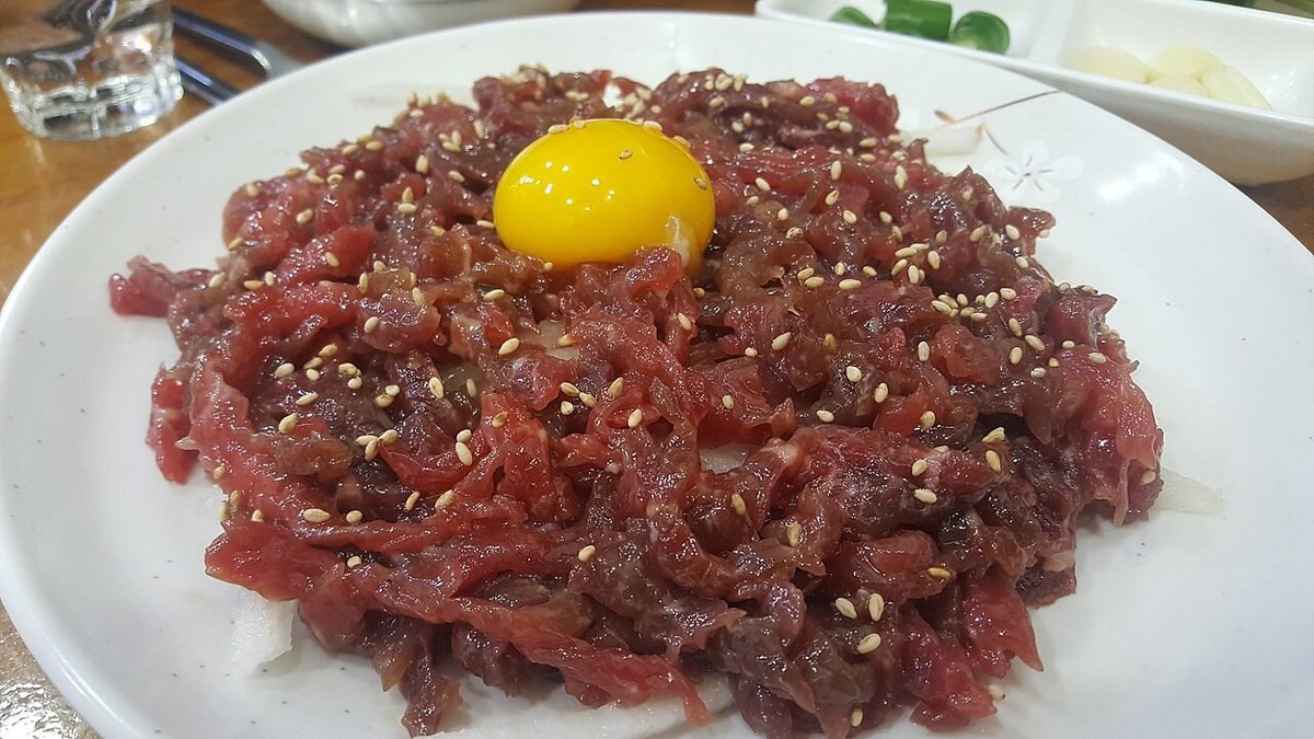 흰 접시에 수북이 담긴 붉은 소고기 육회 위에 달걀노른자와 깨가 올라간 모습