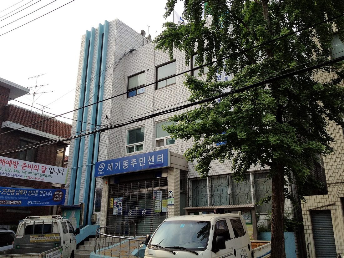 제기동주민센터 파란 간판이 걸린 흰 타일 건물과 그 앞에 세워진 흰색 트럭