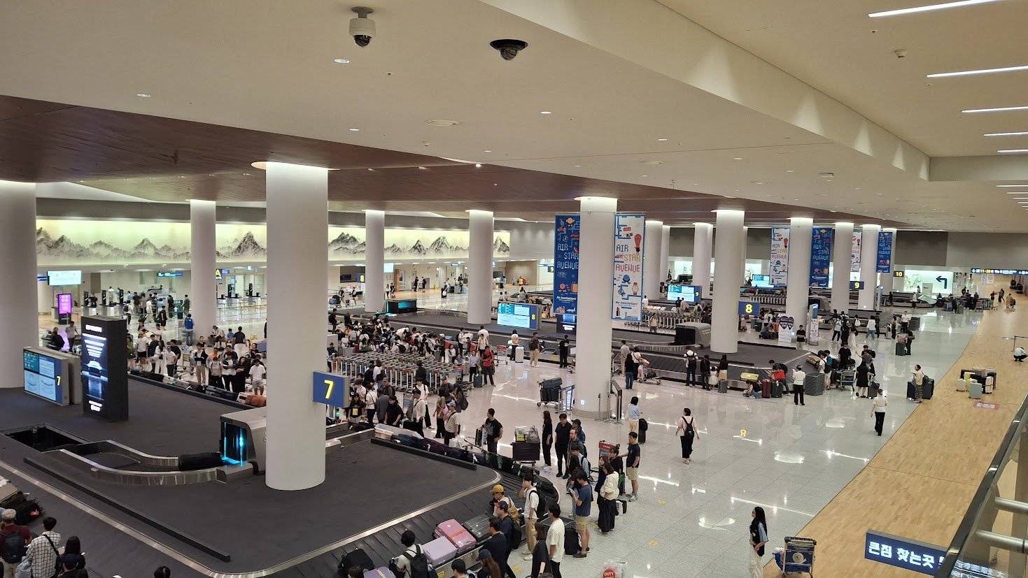 인천공항 제2여객터미널 수하물 수취 구역, 7번 컨베이어 벨트 주변에서 짐을 기다리는 승객들과 흰 기둥