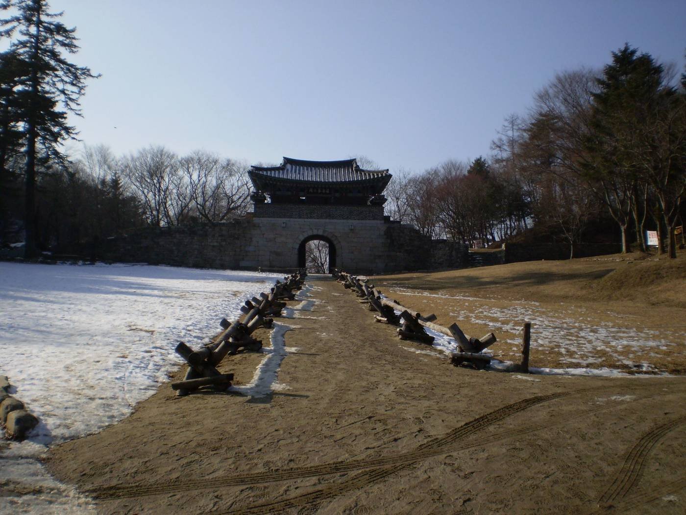 Third gate Joryeonggwan at the end of a dirt path, with wooden rails and patches of snow