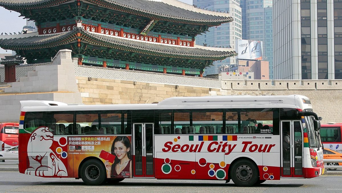 숭례문 성문과 성벽 앞 도로를 지나는 흰색과 빨간색의 Seoul City Tour 1층 버스