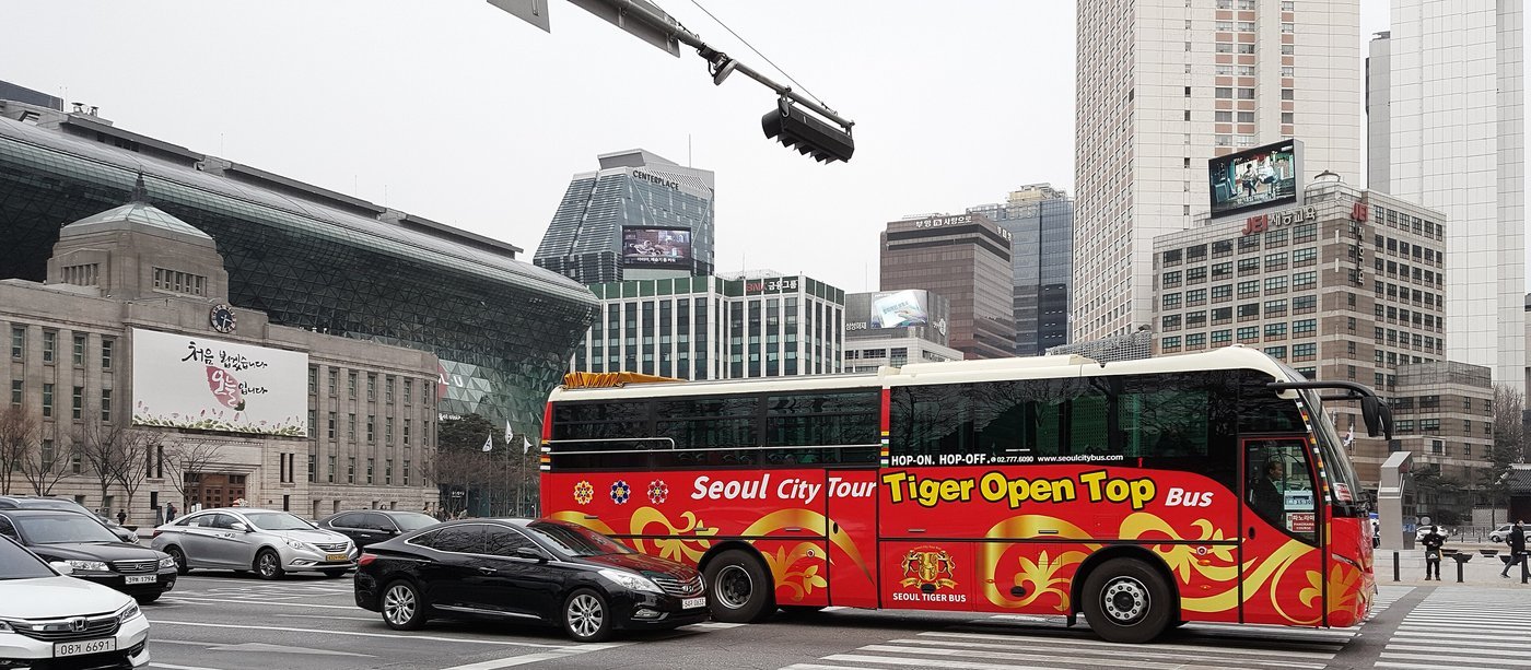 서울시청 본관과 신청사 앞 도로를 지나는 붉은색 바탕에 금색 무늬가 그려진 Tiger Open Top Bus
