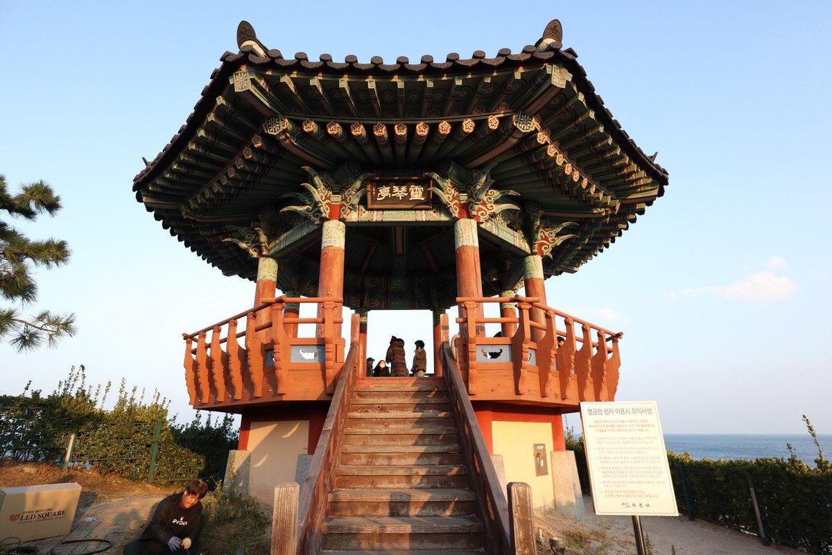 파란 하늘 아래 단청 지붕의 2층 정자와 앞 계단·안내판
